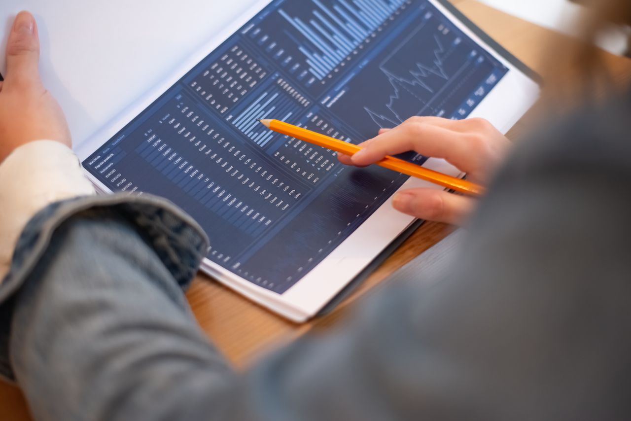 Image rapprochée de mains examinant des graphiques et des tableaux d’entreprise dans un dossier, mettant en avant les analyses de données.